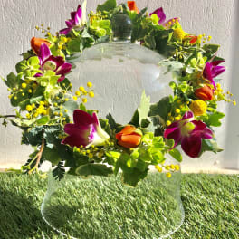 Floral wreath with purple orchids and orange tulips on a glass stand