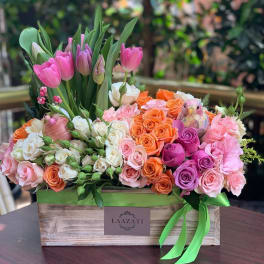 Mixed bouquet of pink tulips and roses in a wooden box with a green ribbon