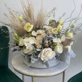 Cream roses and pale yellow tulips in a low gray bowl with dried grasses