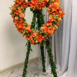 Heart-shaped floral wreath on a stand with orange and pink blooms