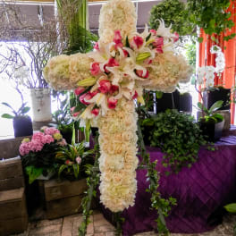Large floral cross on an easel with white lilies, roses, and pink accents