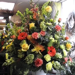Large mixed flower arrangement in a white container with yellow roses and orange blooms