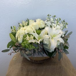 White floral arrangement with lilies, roses, and hydrangeas in a wooden container