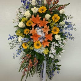 Tall standing floral spray with orange lilies, yellow daisies, and blue flowers