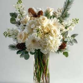 White roses and daisies arranged in a clear glass vase with pinecones and pine sprigs