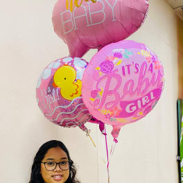 Pink baby girl themed helium balloons held by a woman indoors