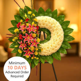 Crescent standing wreath with white blooms, pink lilies, red and yellow flowers on a green leaf base.
