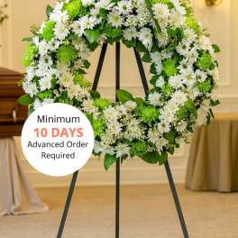 Large white and green floral wreath on a black metal easel in a chapel.