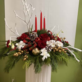 Holiday centerpiece with red roses, white flowers, and red candles in a white pedestal vase