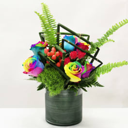 Rainbow roses with red spray roses and ferns in a green vase with geometric bamboo accents