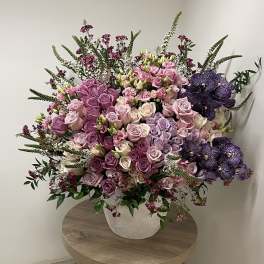 Large arrangement of pink and lavender roses with purple orchids in a white pot on a table