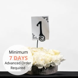 Low round arrangement of white roses and carnations in a box with a table number card.
