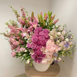 Large pink and white flower arrangement with roses and lilies in a white pot on a table