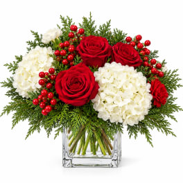 Red roses and white hydrangeas in a clear square vase with berries