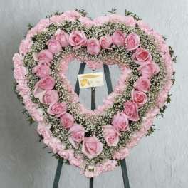 Heart-shaped pink rose and carnation floral wreath on an easel
