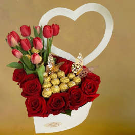 Heart-shaped white box with red roses, red tulips, and gold-wrapped chocolates.