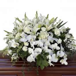 Large white casket spray of lilies, roses, carnations, and orchids on a wooden casket.