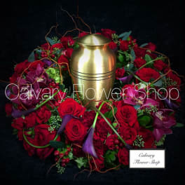 Red rose and orchid wreath around a gold urn on a black background