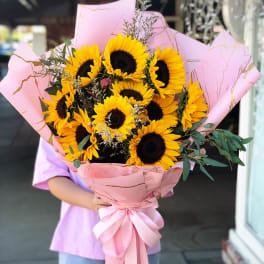 Large bouquet of sunflowers wrapped in pink paper with a ribbon