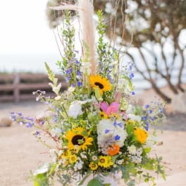 Tall mixed flower arrangement in a white container with sunflowers and lilies