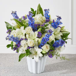 White lilies, roses, and blue-purple flowers in a white vase
