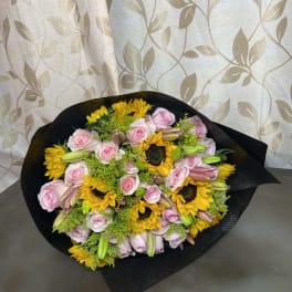 Bouquet of pink roses, sunflowers, and lilies wrapped in black paper