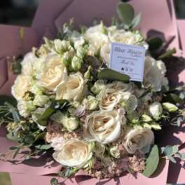 Bouquet of cream roses and small white blooms wrapped in pink paper
