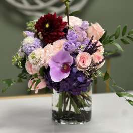 Mixed pink, purple, and burgundy flowers arranged in a clear glass vase