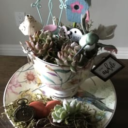 Succulent arrangement in a floral teacup with birdhouse and decorative accents