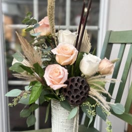 Peach and white roses with dried accents in a tall white ceramic vase