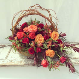 Basket arrangement of orange and red roses with mixed foliage