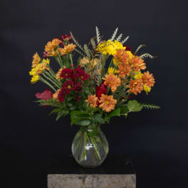 Mixed bouquet of orange, yellow, and red flowers in a clear glass vase