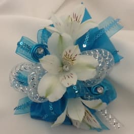 White flowers with blue ribbon and silver accents arranged in a small bouquet