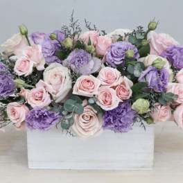 Low arrangement of pink roses and lavender lisianthus in a white wooden rectangular box