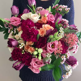 Large bouquet of pink, purple, and peach flowers held by a person