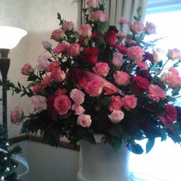 Large pink and red rose arrangement in a white pedestal vase