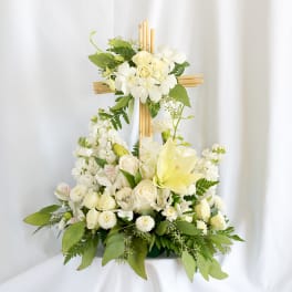 White floral arrangement on a wooden cross with lilies and roses
