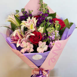 Bouquet of red roses and pink lilies wrapped in pink and purple paper