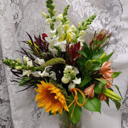Mixed bouquet with sunflowers, white snapdragons, and lilies in a glass vase