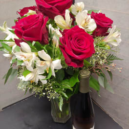 Bouquet of red roses and white alstroemeria in a glass vase with a wine bottle