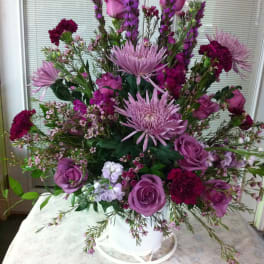Purple floral arrangement in a white container with roses and tall blooms