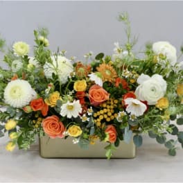 Low floral arrangement in a rectangular vase with white, orange, and yellow blooms