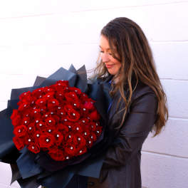 Woman holding a large bouquet of red roses wrapped in black paper