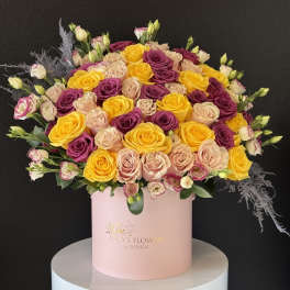Large bouquet of yellow, blush, and purple roses in a pink hat box