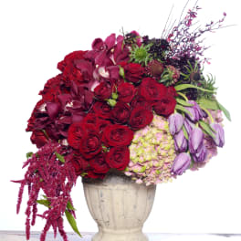 Large bouquet of red and purple flowers in a cream urn vase