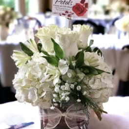 White floral arrangement in a square glass vase with a ribbon