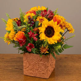 Mixed bouquet with sunflowers, orange roses, and red alstroemeria in a square vase