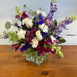 Mixed bouquet in a square glass vase with white, purple, and pink flowers