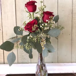 Three red roses in a clear glass vase with white filler flowers