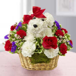 White teddy bear in a basket surrounded by red, white, and purple flowers